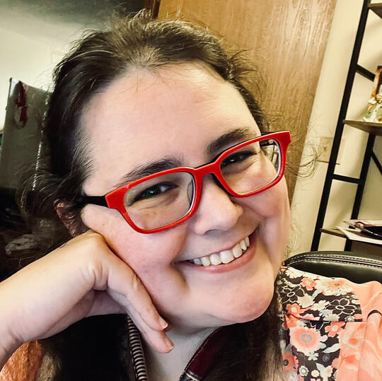 Anastasia Morgan, smiling with red glasses on Anastasia Morgan, game writer, narrative designer, novelist, short story writer, inkslinger